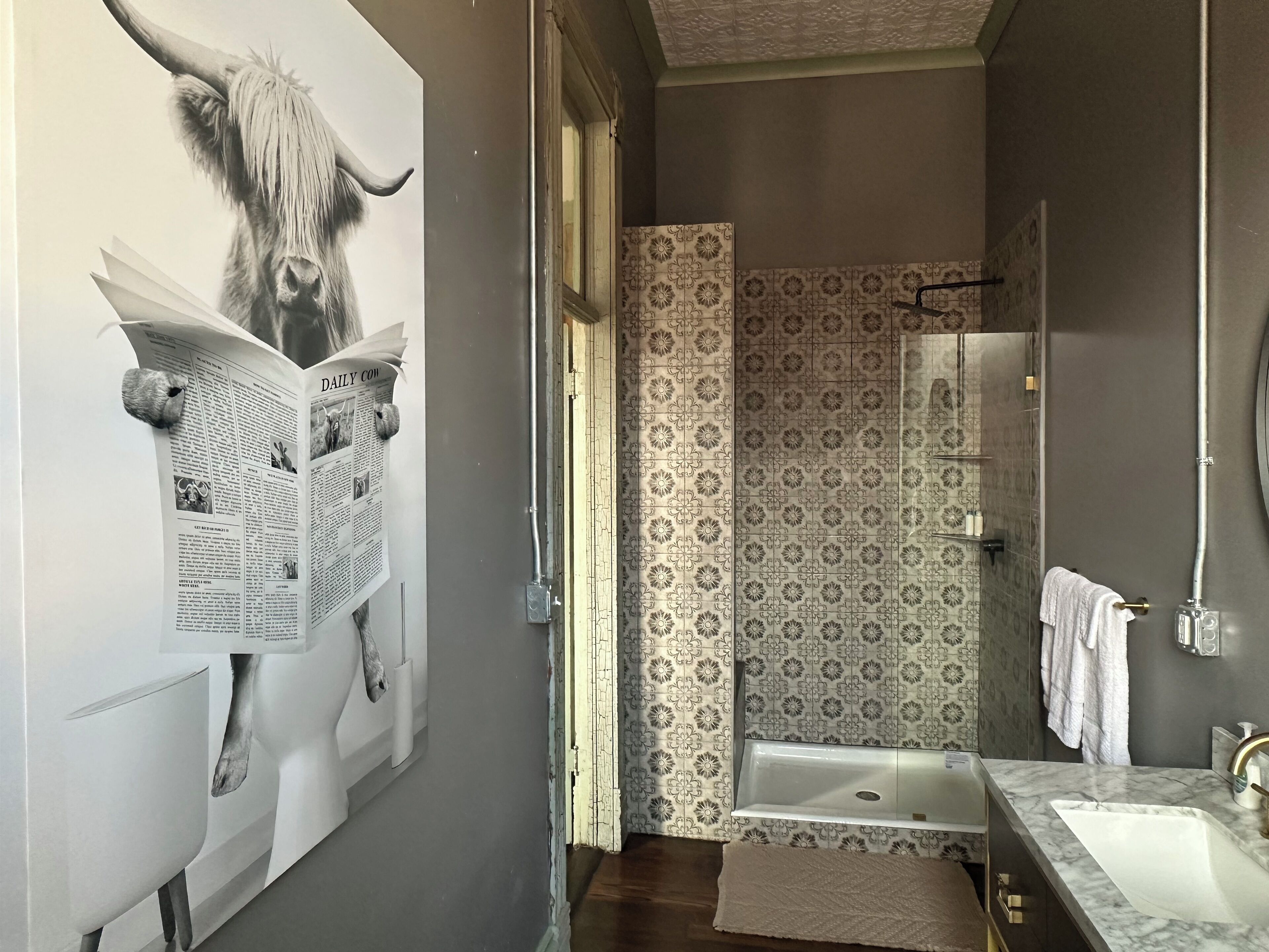 A narrow bathroom with a shower, a sink, and a towel rack.