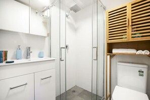 Une salle de bain moderne avec une douche à parois de verre, des meubles blancs et une étagère en bois où sont posées des serviettes.