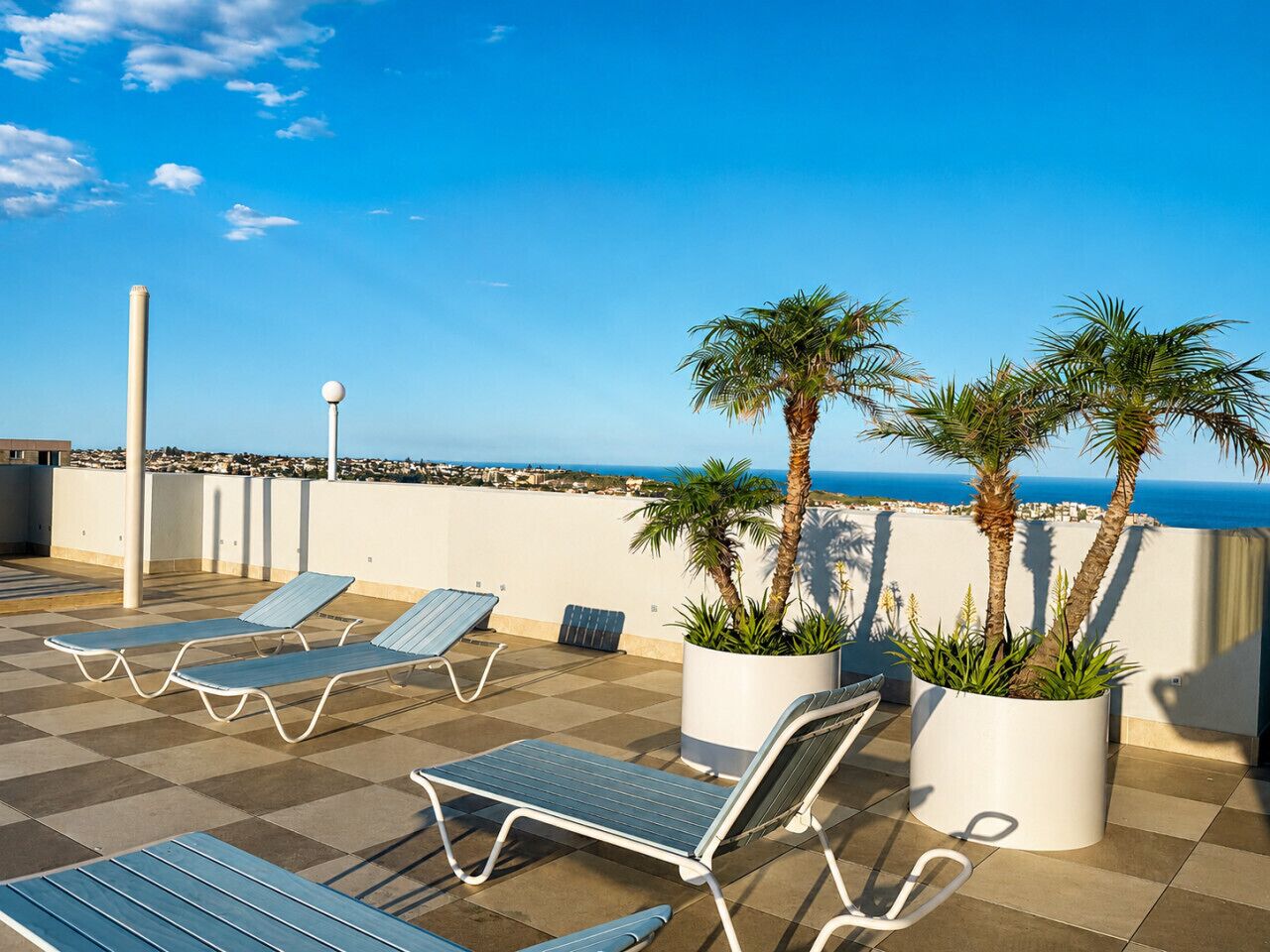 A rooftop terrace with lounge chairs, potted plants, and a view of the sea.