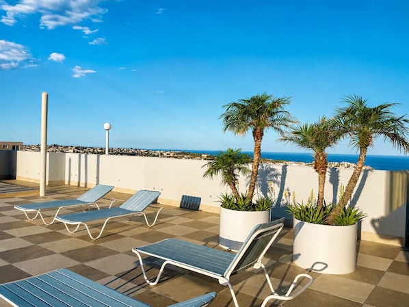Una terraza en la azotea con sillones, plantas en macetas y vistas al mar.