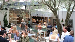 An outdoor dining area with tables and chairs, surrounded by trees and a building with a kitchen visible in the background. - Stylish Bondi Studio Minutes From Bondi Beach (Bondi)