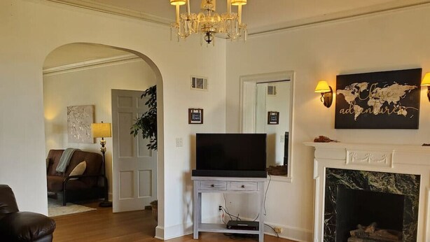 Una sala de estar con chimenea, televisor sobre un mueble bajo y una araña.
