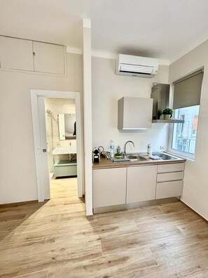 Een koelkast, een waterkoker, kookgerei, borden en bestek, eettafels