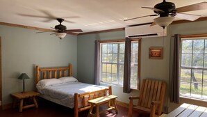 A bedroom with a wooden bed, a wooden chair, a wooden table, a ceiling fan, and a window with curtains.