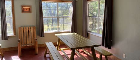 A room with a wooden table and benches, large windows, a ceiling fan, and an air conditioning unit.