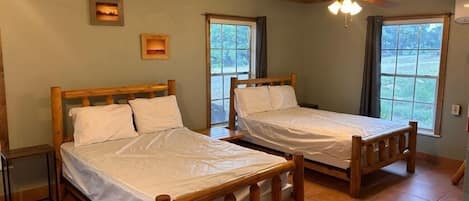 A room with two wooden beds, a ceiling fan, and large windows.
