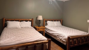 Una habitación con dos camas de madera, un ventilador de techo y una mesita de noche con lámpara.