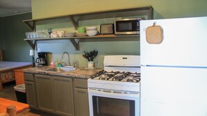 Eine Küche mit Gasherd, Backofen, Mikrowelle und Spüle. Über der Spüle befinden sich Regale mit Geschirr und Gläsern.