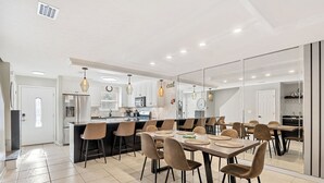 A modern kitchen with a central island, bar stools, and a dining area with a large table and chairs. - Steps to Beach - 2 MBR-2.5 Bath, Sleeps 6, Gulf Highlands Beach Resort Townhome (Panama City Beach)