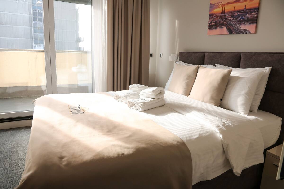 Ein Hotelzimmer mit Bett, einem Fenster mit Vorhängen und Blick auf die Stadt.