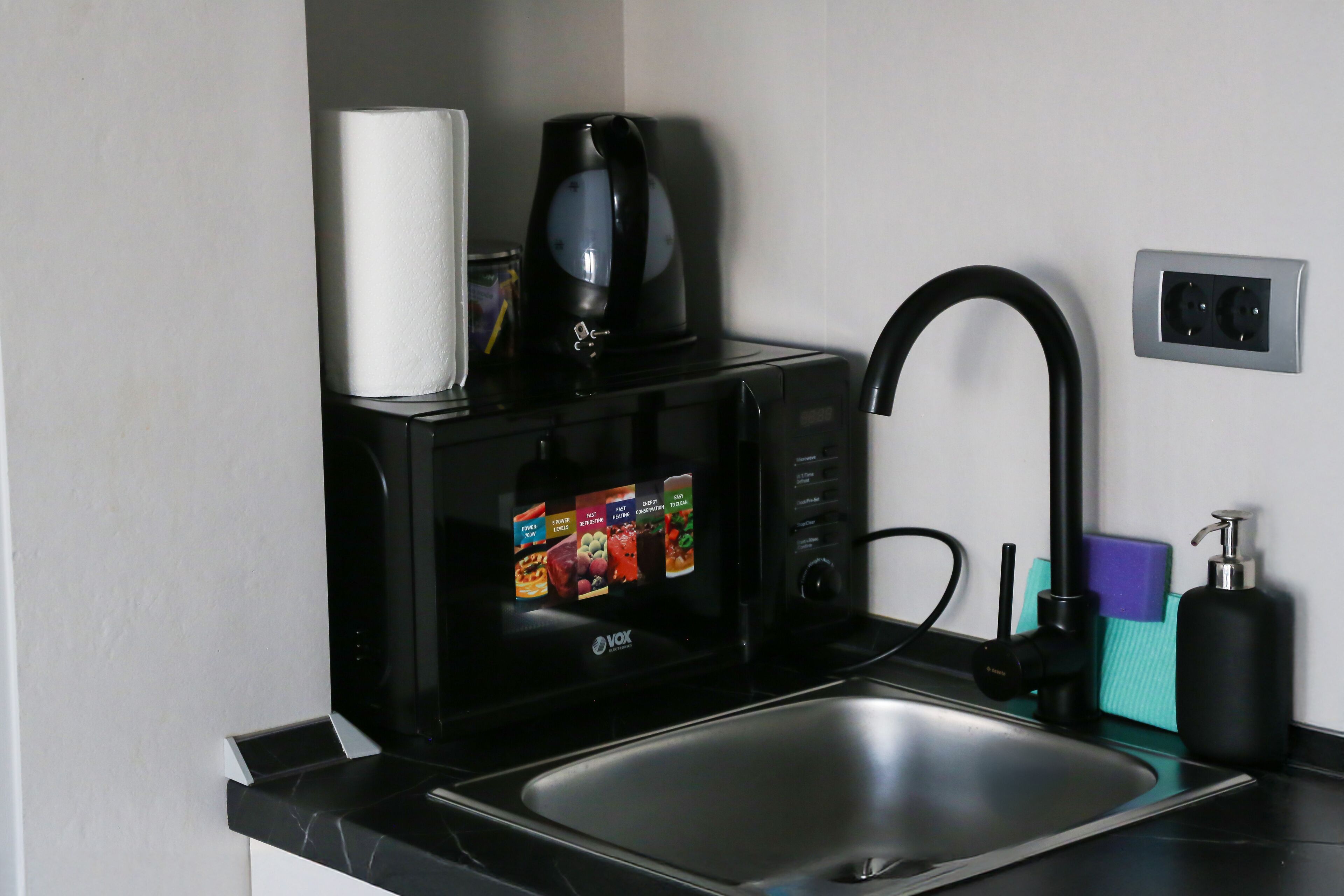 Ett kök med mikrovågsugn, kaffebryggare, diskho och tvålpump.