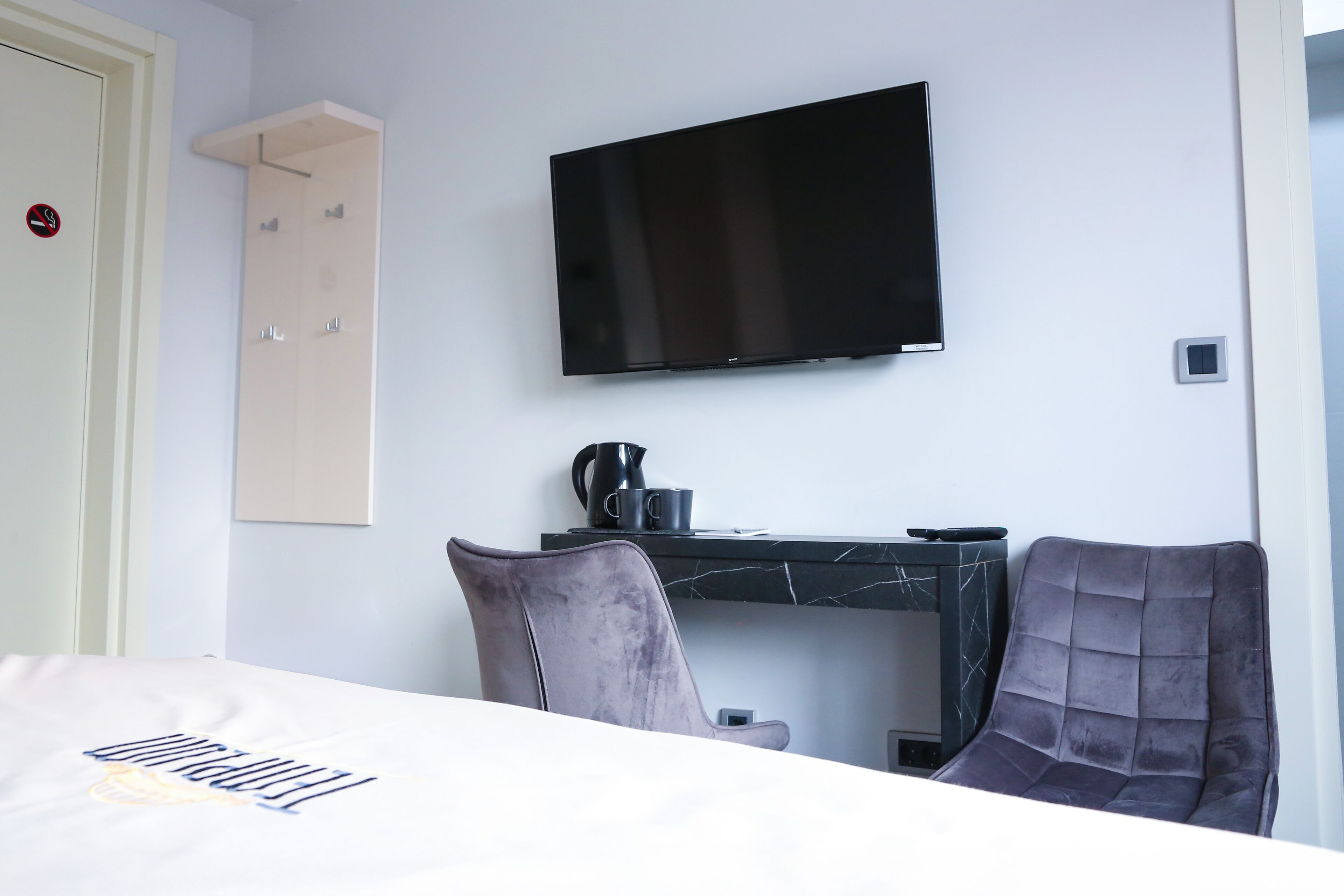 A hotel room with a bed, a desk with a flat-screen TV, a chair, and a wardrobe.