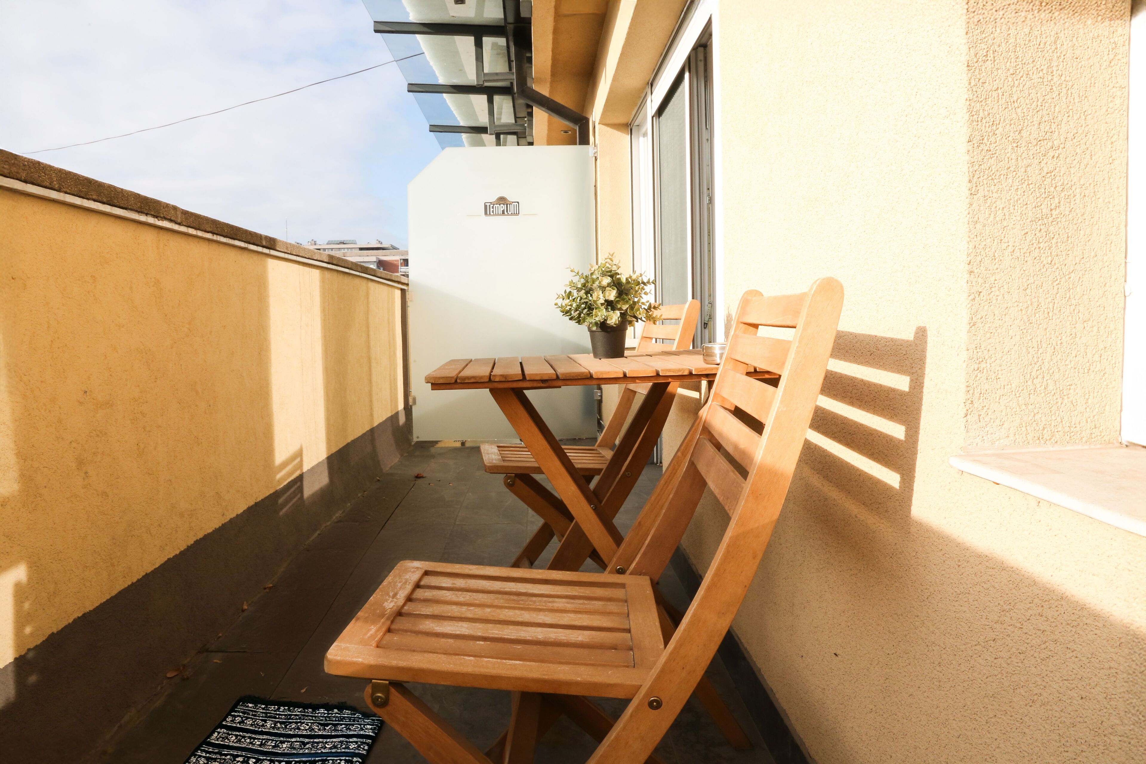 Una mesa y sillas de madera en un balcón, con una planta en maceta.