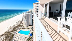 A high-rise hotel with a balcony overlooking a beach and a pool.