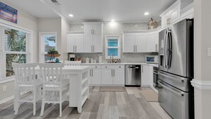 A modern kitchen with white cabinetry, stainless steel appliances, and a dining area with white chairs. - Ocean Lakes Walk to Beach! Waterpark! Arcade! Dogs Welcome! (Myrtle Beach)