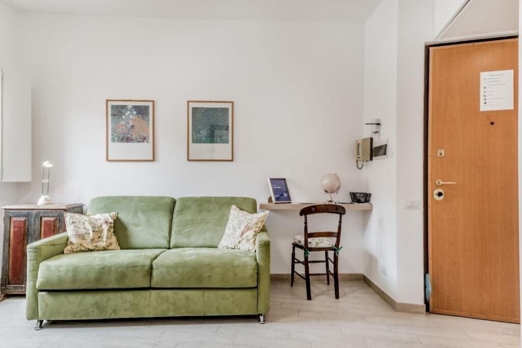 A room with a green sofa, two framed pictures on the wall, a wooden door, and a small table with a globe.