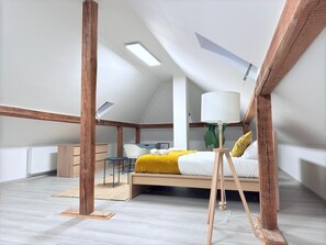 A modern loft bedroom with a sloped ceiling, exposed wooden beams, a bed with a yellow throw, a standing lamp, and a radiator. - Spacious 4 bedrooms House (Strassen)