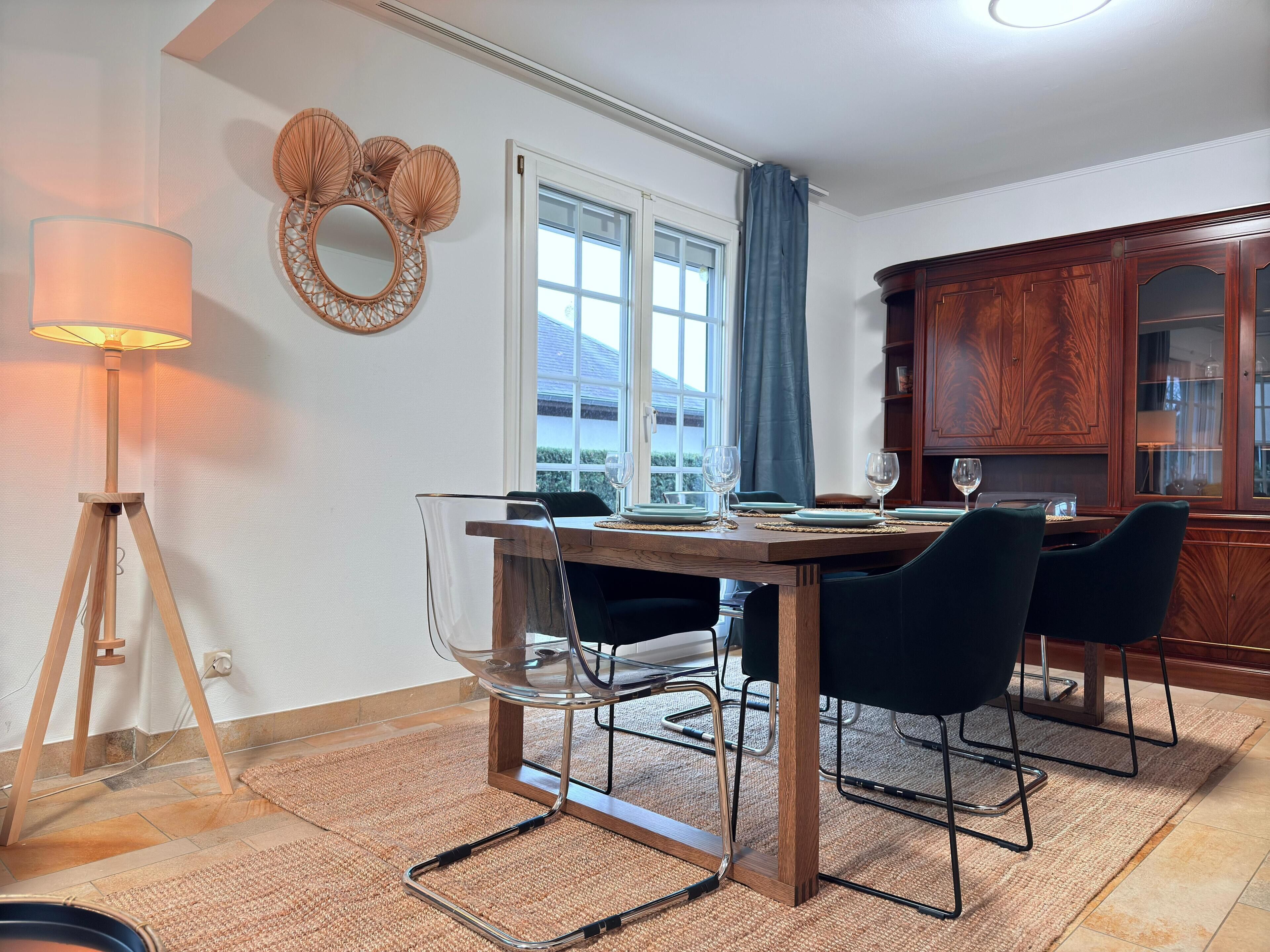 Un coin repas avec une table en bois, des chaises transparentes, une lampe et une fenêtre avec des rideaux.