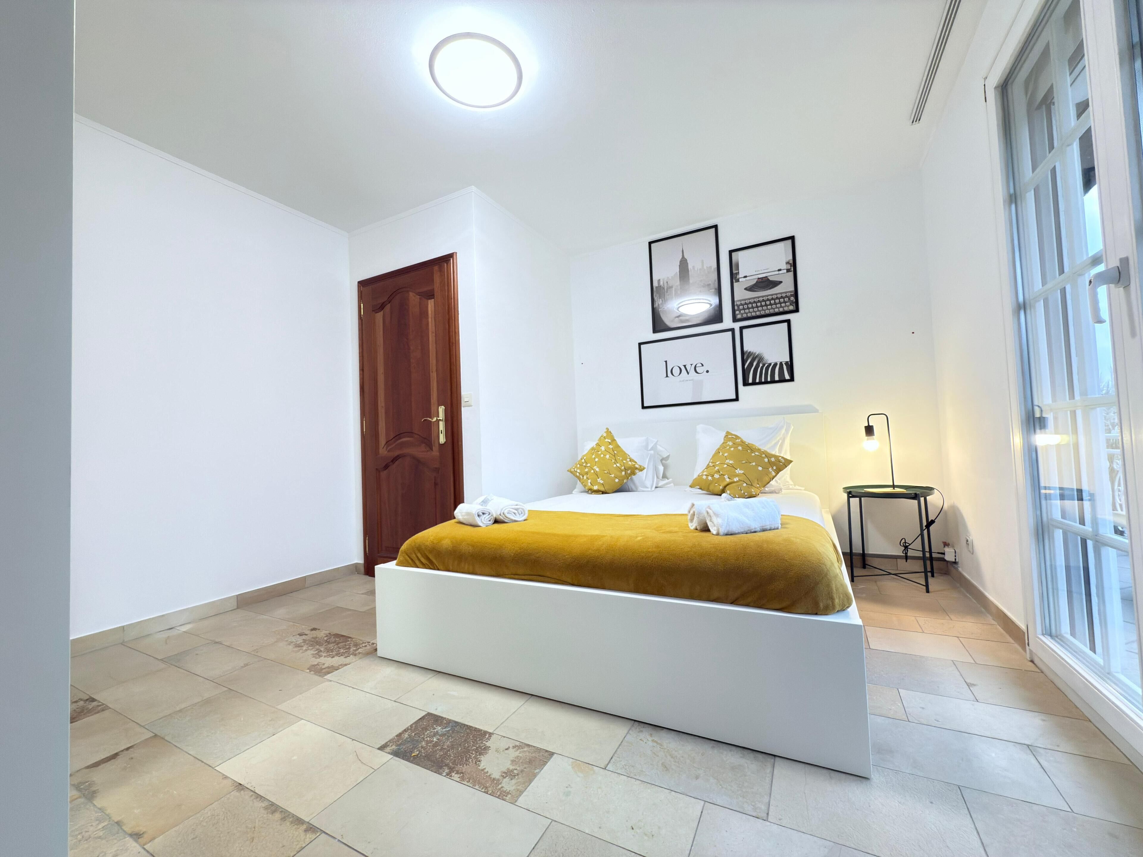 A modern bedroom with a large bed, a wooden door, and a window.