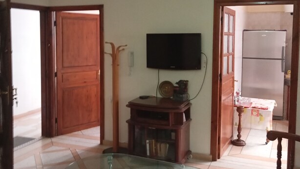 Ein Wohnzimmer mit Fernseher, einem Glastisch, einer Holztür und einem Fliesenboden.