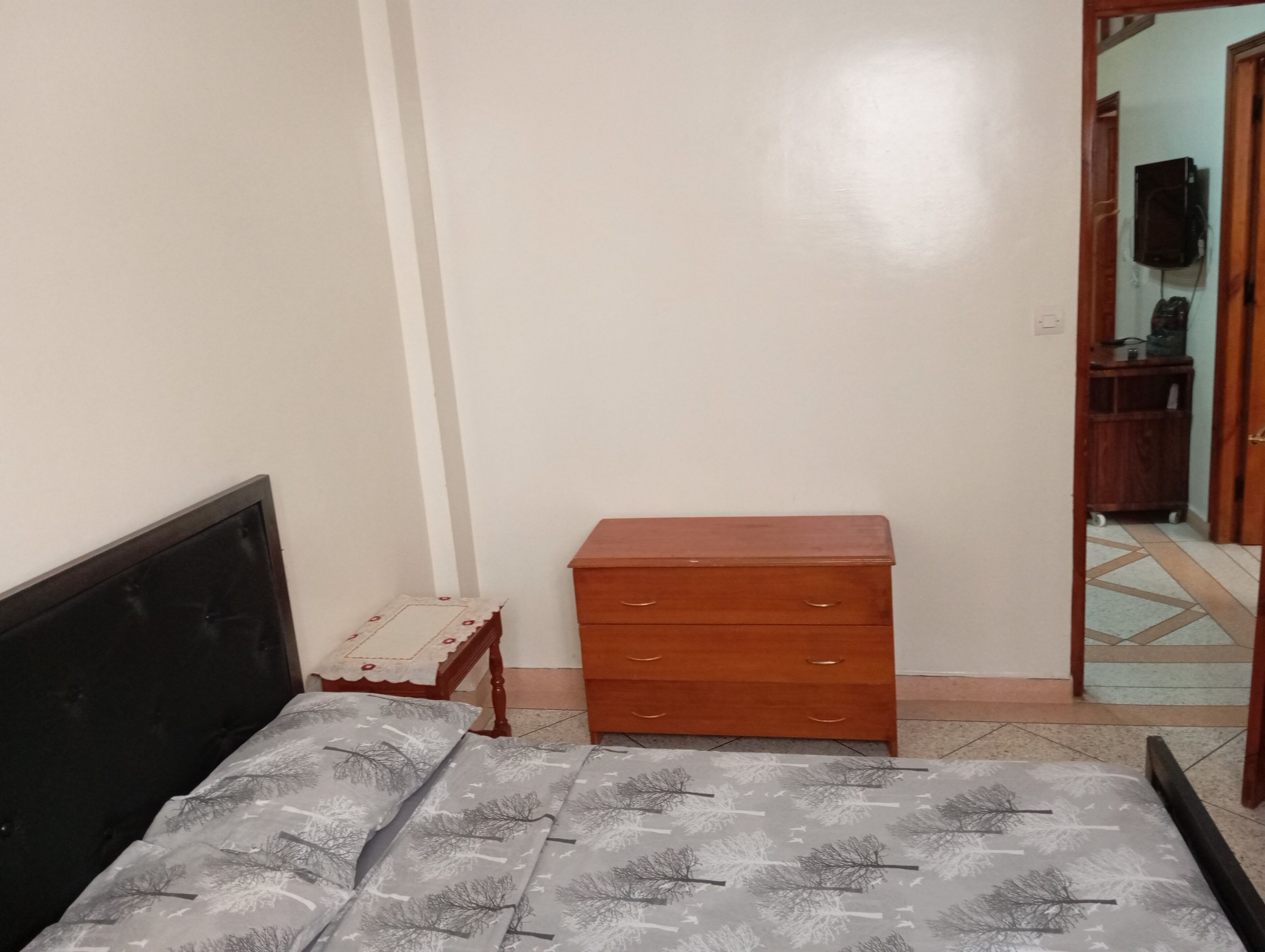 A bedroom with a bed, a wooden dresser, and a small table.