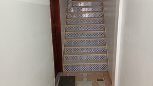 Ein schmaler Flur mit Fliesenboden und geometrischen Mustern, auf der linken Seite eine Holztür.