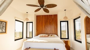Ein Schlafzimmer mit einem Bett, einem Deckenventilator und großen Fenstern.