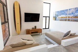 Una habitación moderna con cama, sofá, televisor y una tabla de surf.