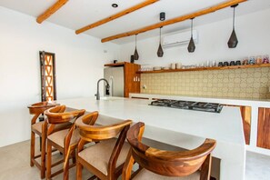 Una cocina moderna con una isla central, sillas de madera, horno empotrado e iluminación colgante.