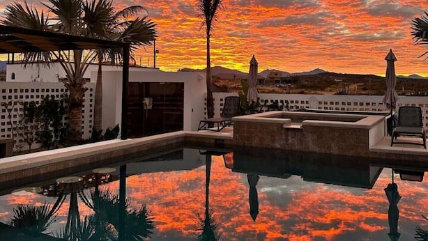 Ein Pool auf dem Dach mit Blick auf einen Sonnenuntergang über einer Wüstenlandschaft.
