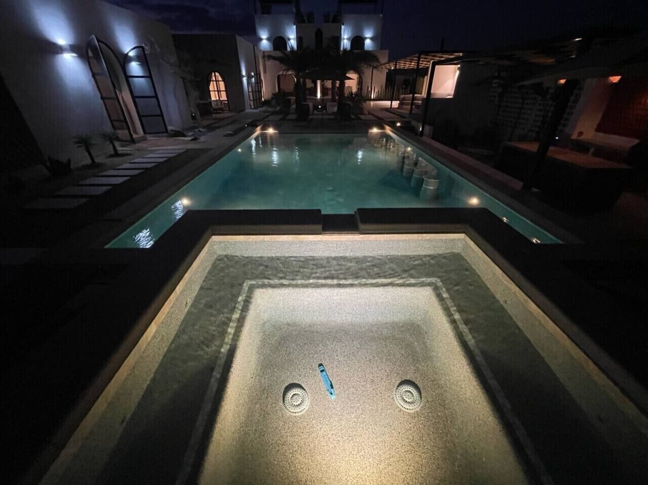 Une piscine avec un jacuzzi au centre, entourée de chaises longues et d’un espace salon abrité.