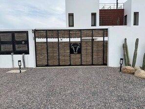 Una entrada con portón cerrado, un portón decorativo, un letrero pequeño y una planta de cactus.