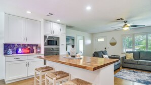 Una cucina moderna con mobili bianchi, un'isola in legno con sgabelli da bar, un forno integrato e un neon.