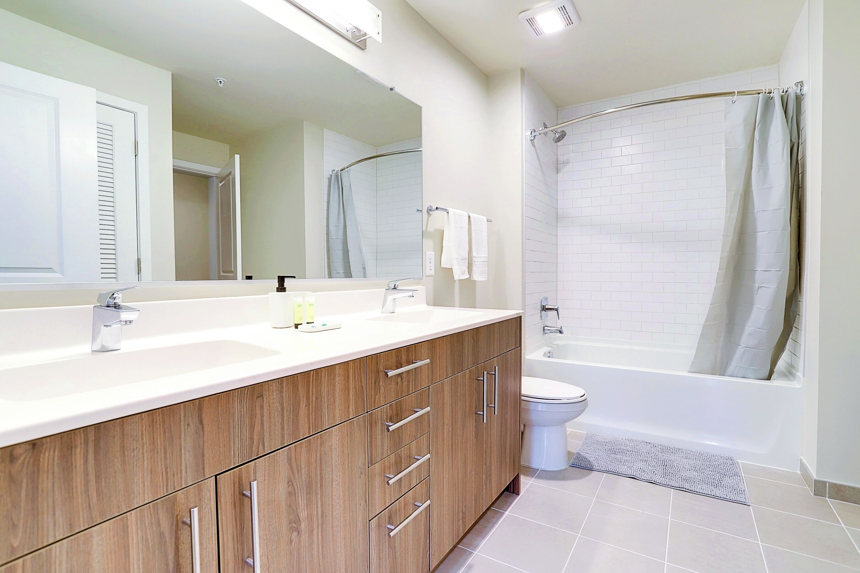 Un baño moderno con tocador de madera, un espejo grande, una bañera y un inodoro.