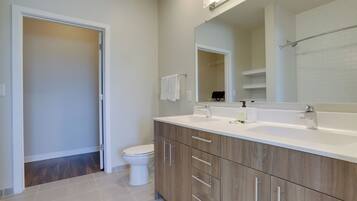 Un baño moderno con inodoro blanco, armarios de madera, un espejo grande y un lavamanos blanco.
