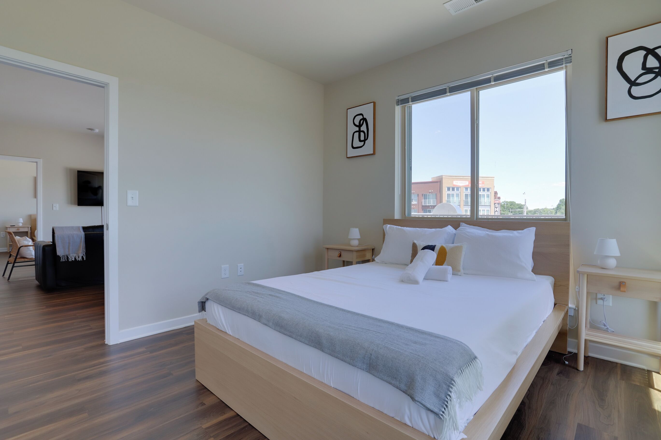 A modern bedroom with a large bed, bedside tables, a TV, and a window with a city view.