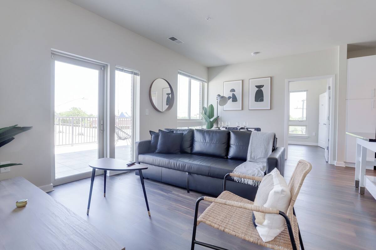 A modern living room with a dark leather sofa, a round mirror, and a wicker chair.