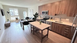 Une cuisine moderne avec des meubles en bois, des appareils électroménagers en acier inoxydable et un coin repas comprenant une table et des chaises.