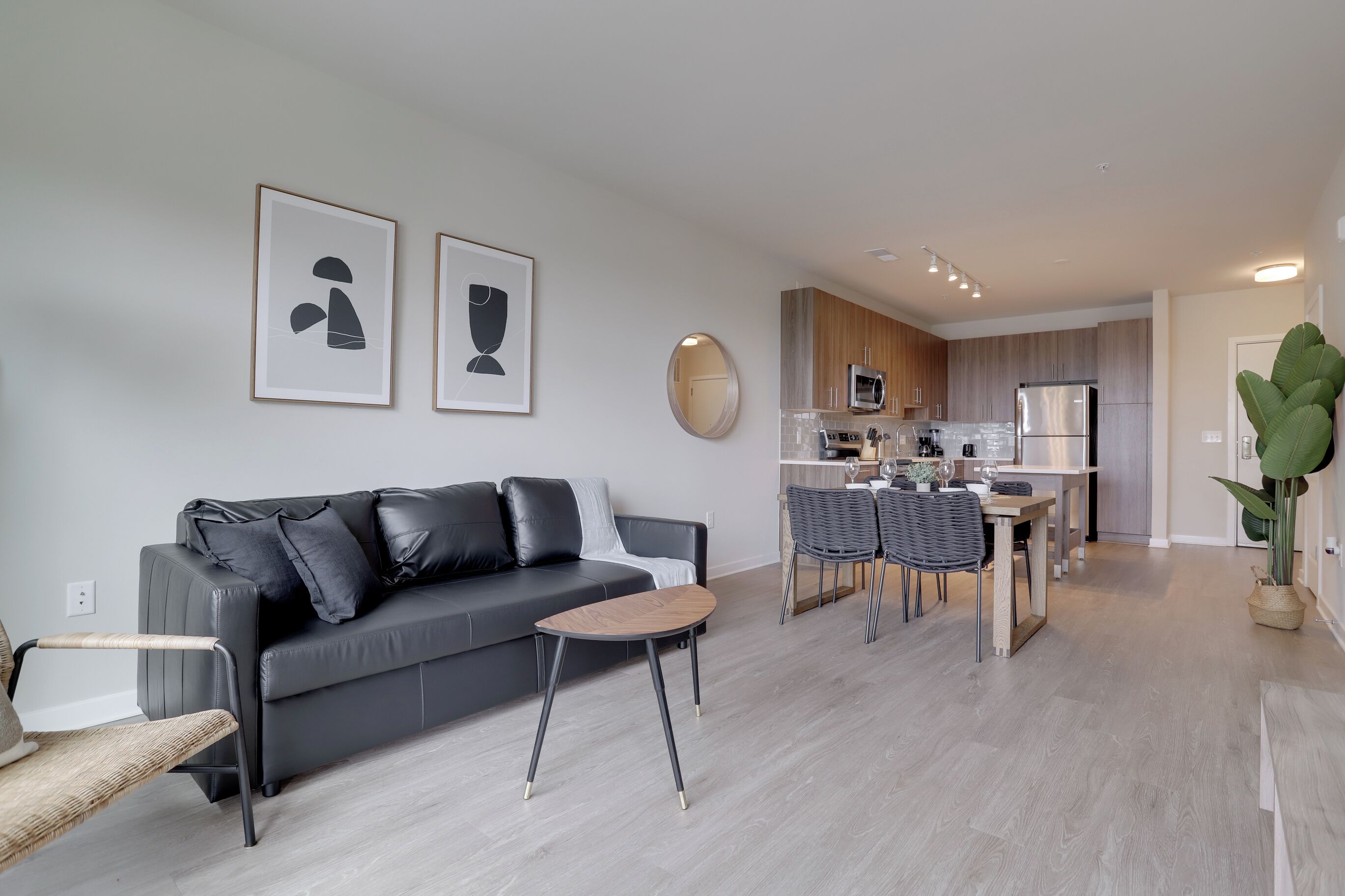 A modern living room with a grey sofa, a small wooden coffee table, and a dining area with a kitchen in the background.
