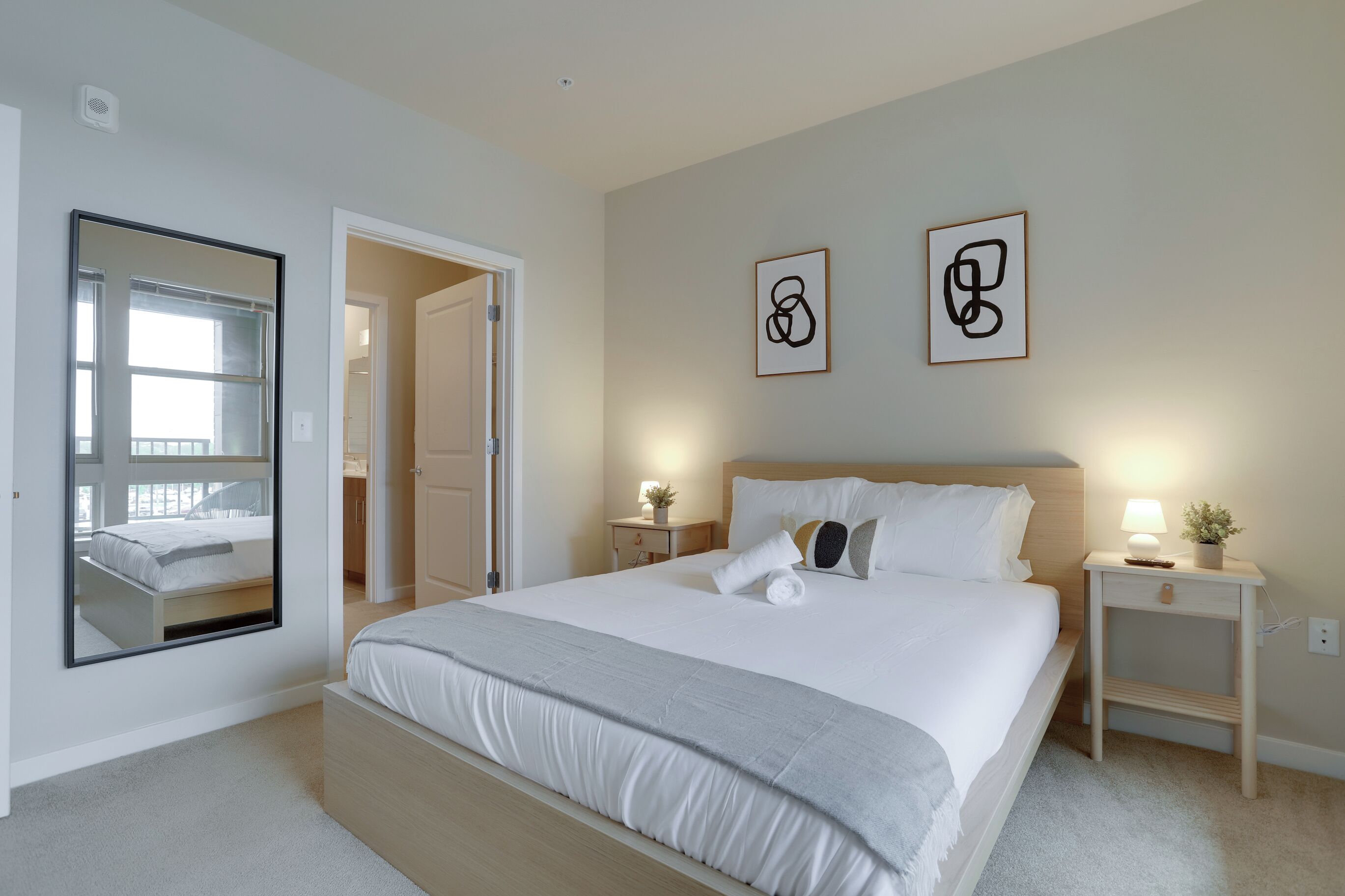 Un dormitorio ordenado con una cama grande, mesitas de noche, un espejo y dos cuadros enmarcados en la pared.