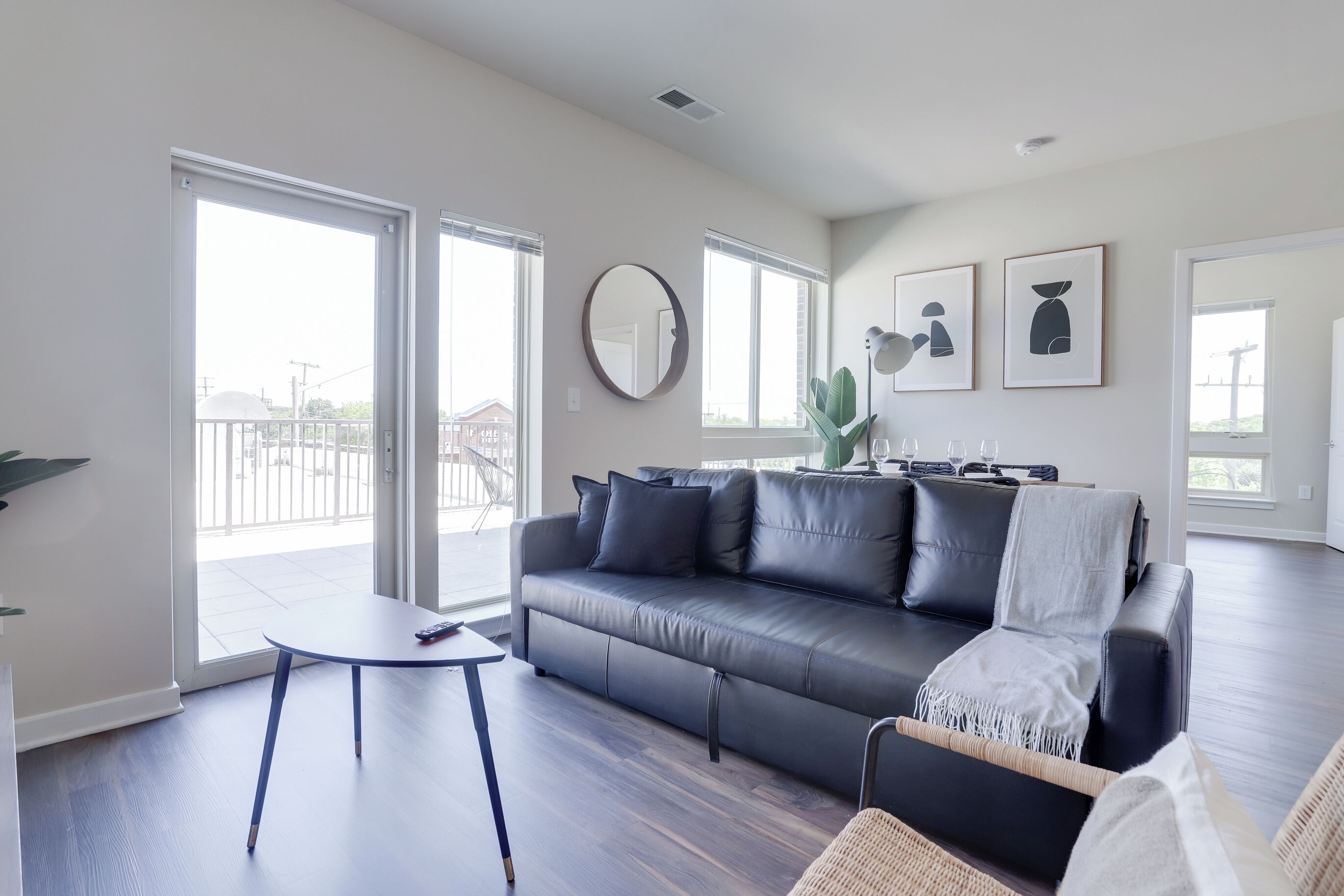 A modern living room with a black leather sofa, a round mirror, and a dining table.