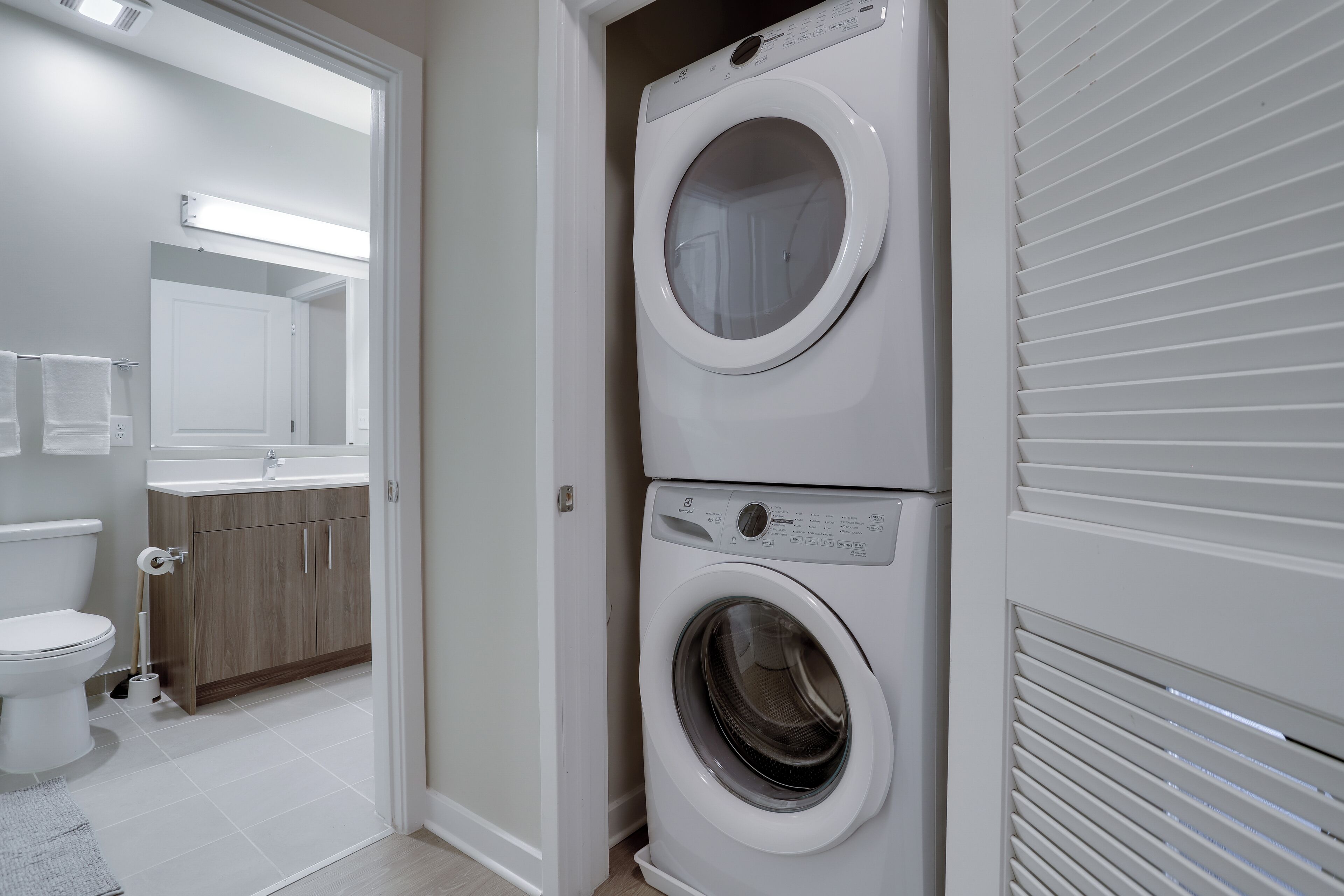 Een wasserette met twee gestapelde wasmachines, een toilet en een wastafel.