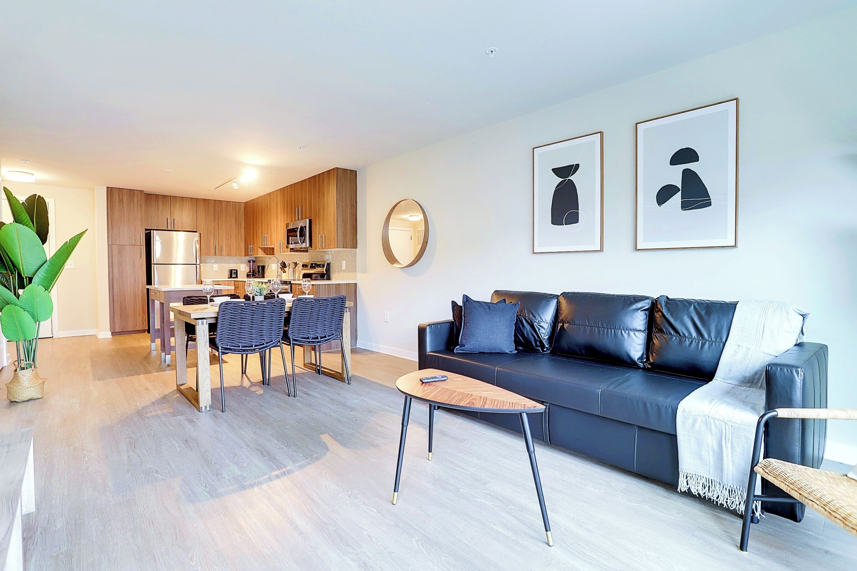 A modern living room with a dark leather sofa, a coffee table, and a dining area with a wooden table and chairs.