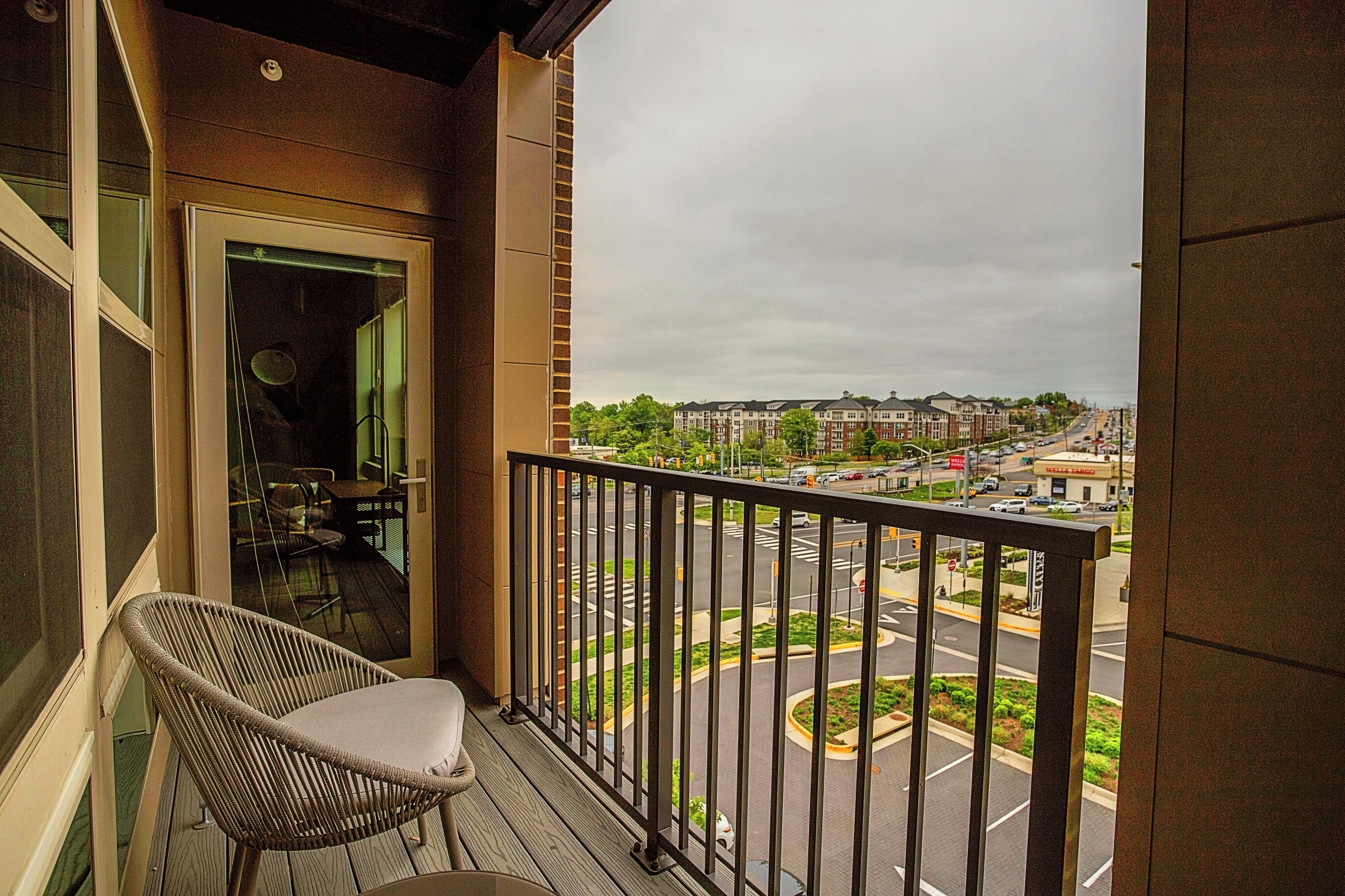 A balcony with a wicker chair and a view of a cityscape with buildings and a roundabout.