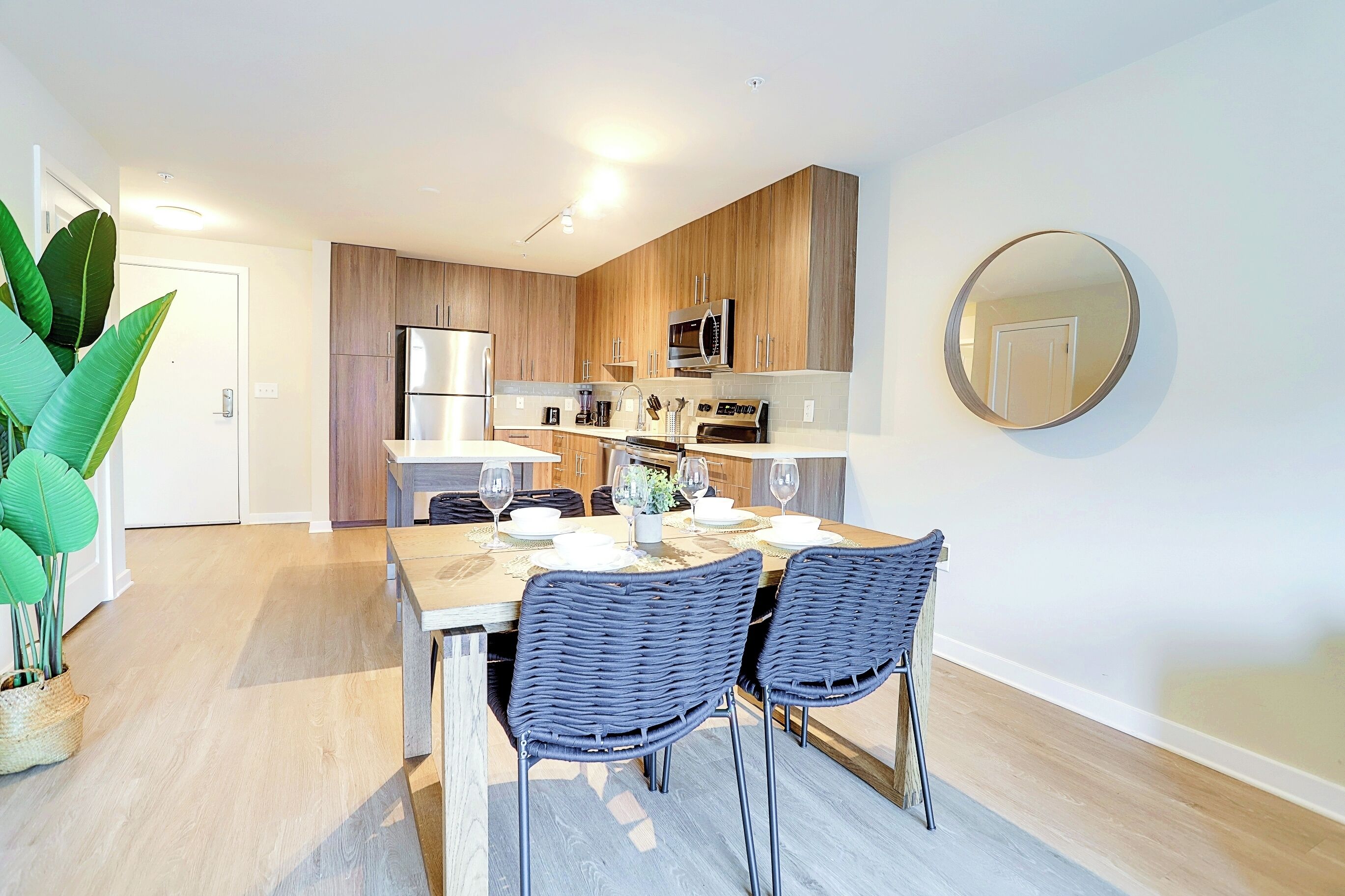 Una cocina moderna con armarios de madera, electrodomésticos de acero inoxidable y un comedor con sillas de mimbre y una mesa dispuesta para dos personas.