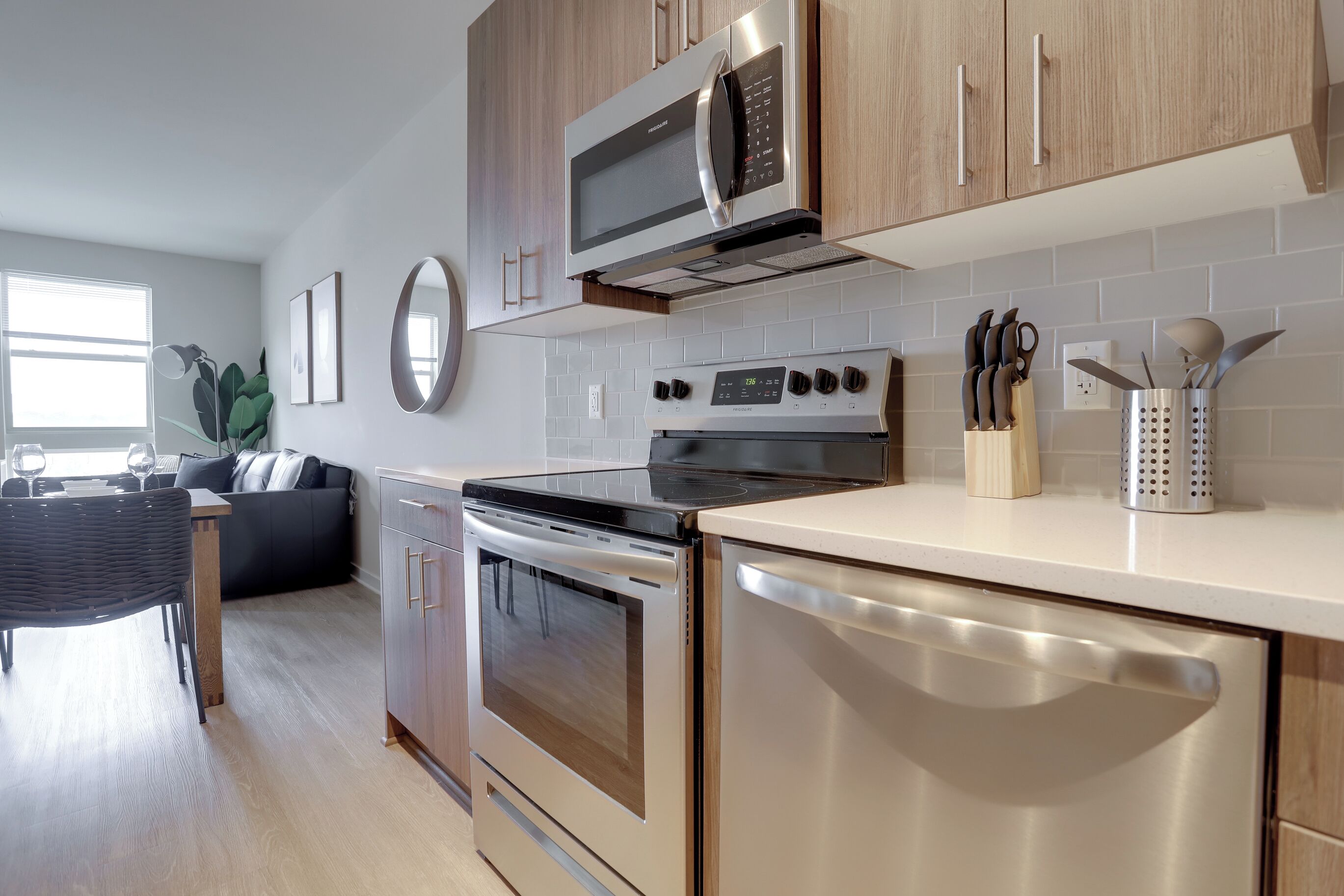 A modern kitchen with stainless steel appliances, wooden cabinets, and a dining area with a black sofa and a dining table.