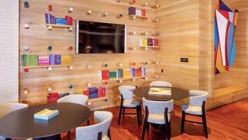 A modern room with a wooden wall, bookshelves, a flat-screen TV, and round tables with chairs.