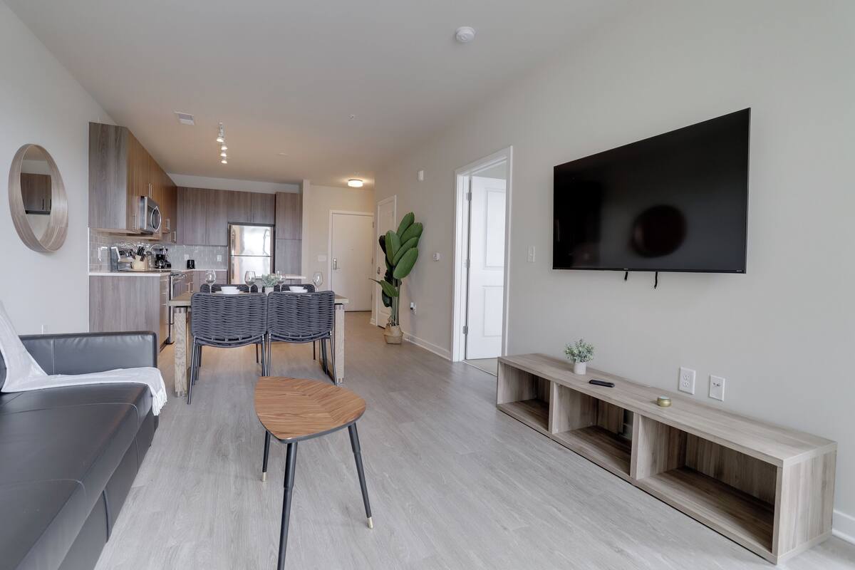 A modern living room with a dining area, kitchen, and a TV mounted on the wall.