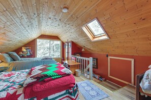 Una camera da letto mansardata accogliente, con tetto in legno spiovente, un lucernario, un letto con una coperta dai colori vivaci, un tavolino e una libreria.