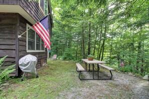 Una baita di legno con una bandiera americana, un tavolo da picnic con un cesto e una sedia in una zona boschiva.